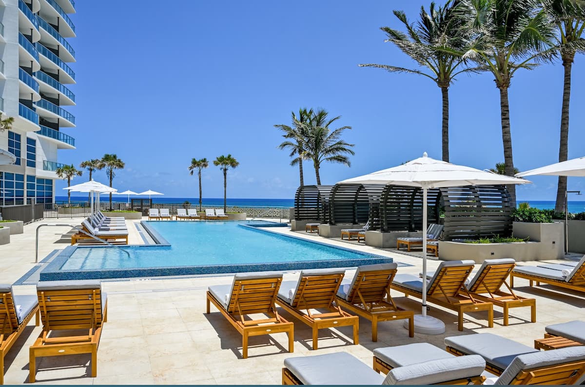 Oceanfront pool lined with palms, sun loungers and umbrellas