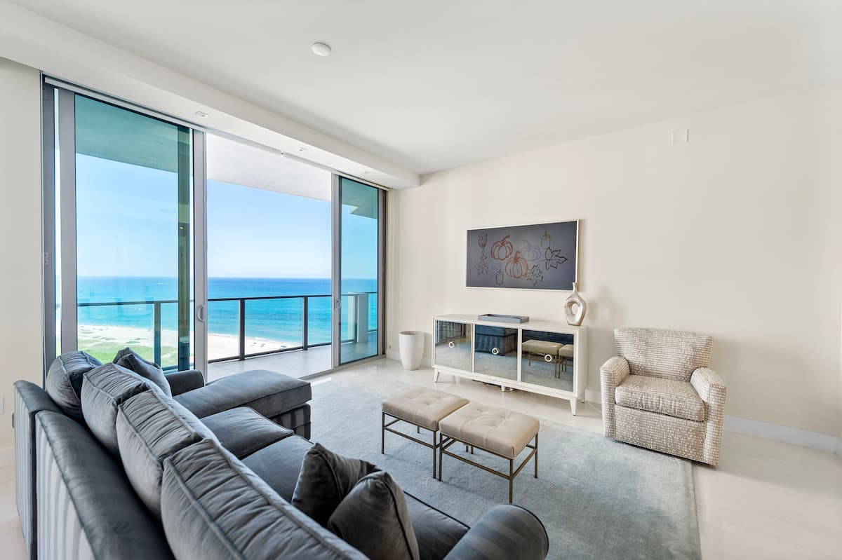 Living room with a deep sectional sofa facing floor-to-ceiling windows and the balcony, the Atlantic beyond